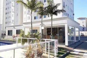 A modern building with a swimming pool, palm trees, and a gated entrance.