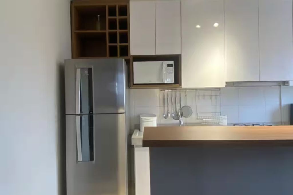 Une cuisine moderne avec un réfrigérateur en acier inoxydable, des armoires blanches et un plan de travail en bois.