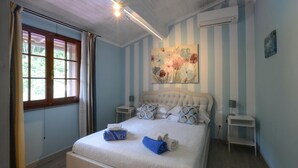 Een slaapkamer met een bed, twee nachtkastjes, een raam met gordijnen, een airconditioner en een bloemendecoratie aan de muur.
