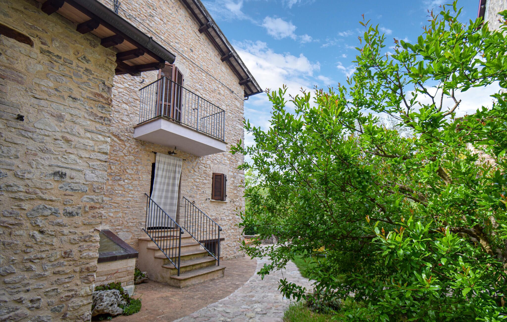 Un bâtiment en pierre doté d’un balcon, d’un escalier et d’un jardin.