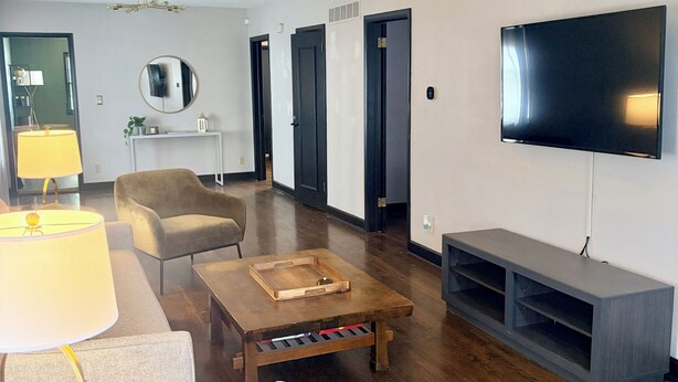 Un salon moderne avec un téléviseur à écran plat, un miroir rond, une table basse en bois et un canapé gris.
