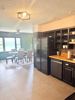 A modern kitchen with a black refrigerator, wooden countertop, and a dining area with chairs and a table.