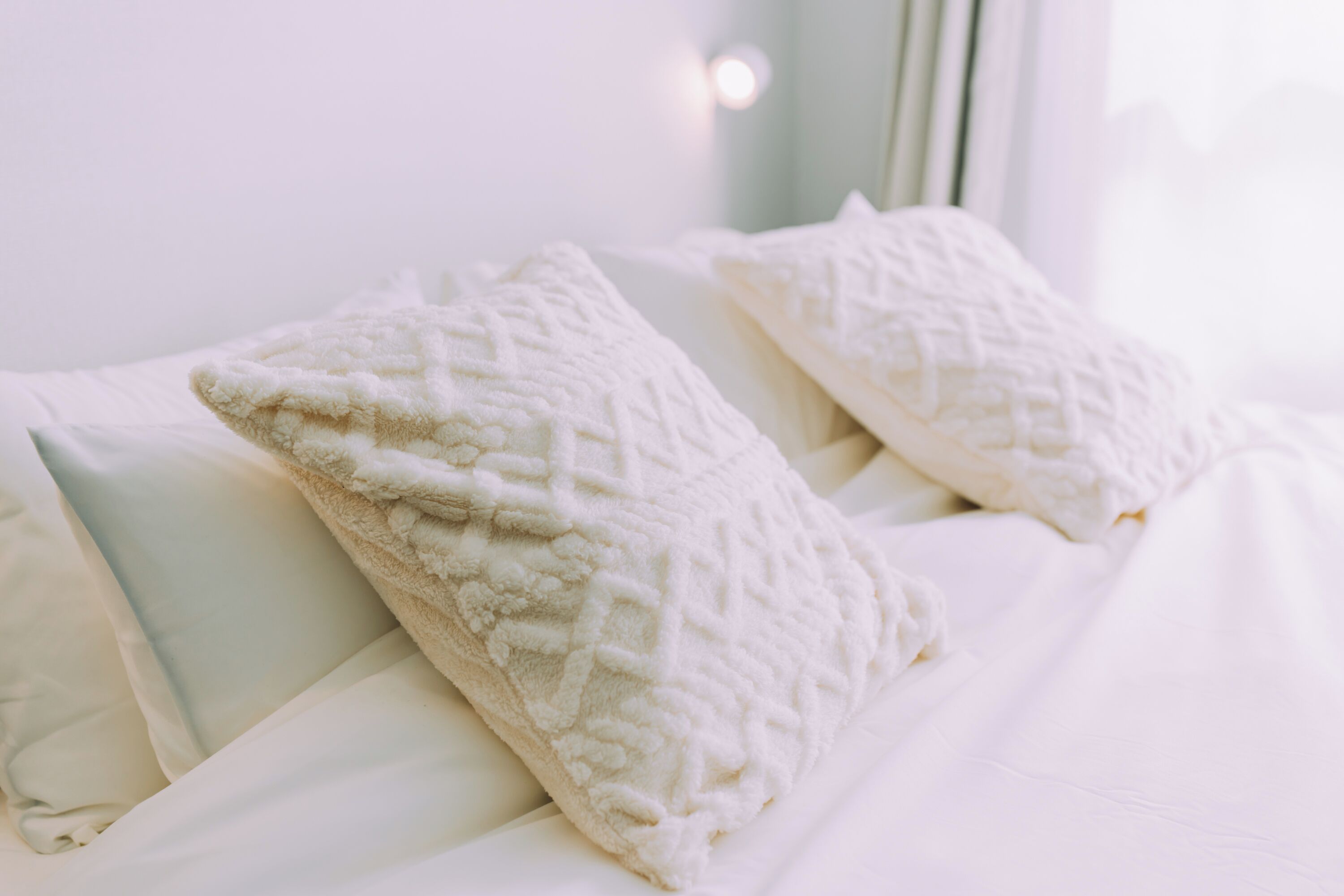 Una cama con ropa de cama blanca y almohadas con textura.