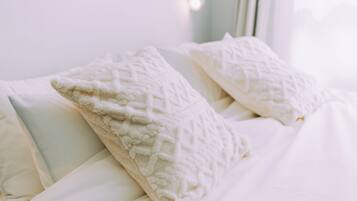 Una cama con ropa de cama blanca y almohadas con textura.