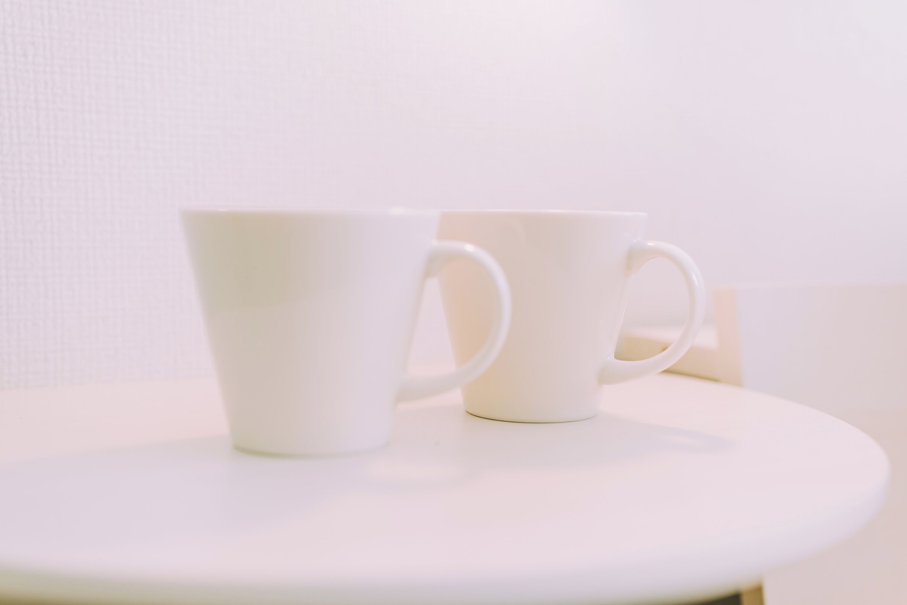 Duas xícaras brancas sobre uma mesa branca, com uma parede branca ao fundo.