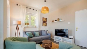 Una sala de estar con sofá, dos sillones, televisor, lámpara y ventana con cortinas.