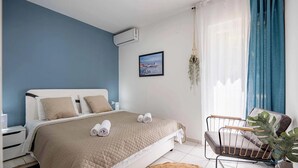 Un dormitorio con una cama, una silla, un cuadro en la pared y un equipo de aire acondicionado.