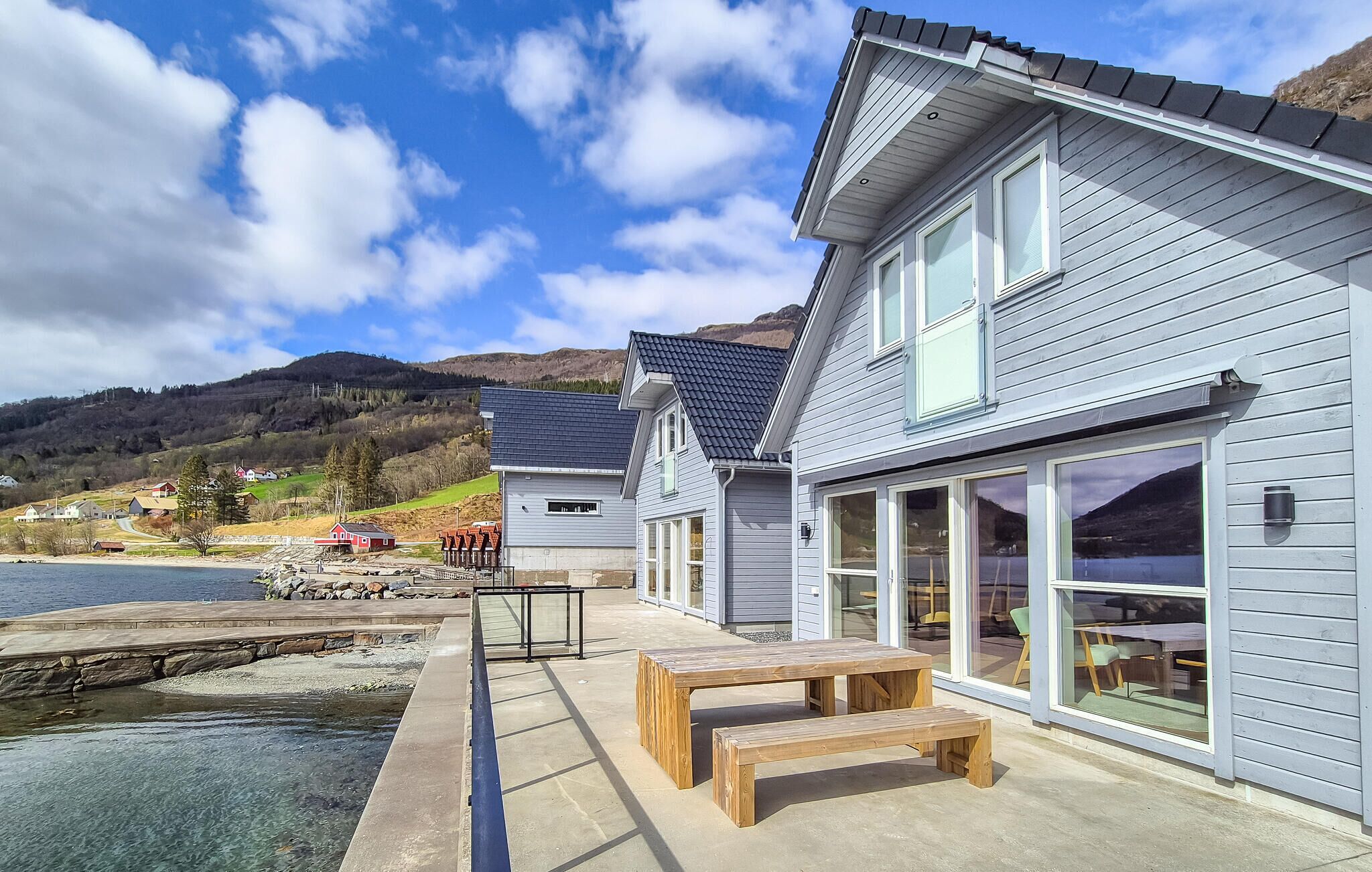 A waterfront property with a large deck, outdoor seating, and a view of the water and hills.