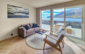 A living room with a sofa, a coffee table, and a chair. There is a large window with a view of mountains and water. - 3 bedroom gorgeous home in Sandeid (Sandeid)