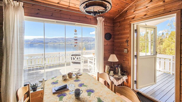 Eine Holzhütte mit Essbereich, einem Tisch mit blumigem Tischläufer und Blick auf einen See.