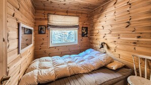 Ein Zimmer in einer Holzhütte mit einem Bett, einem Fenster, einer Lampe und einem Stuhl.