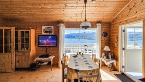 Ein Holzblockhaus-Interieur mit Esstisch, Stühlen, einem Fernseher und Blick auf die Berge durch große Fenster.