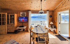 A wooden cabin interior with a dining table, chairs, a television, and a view of the mountains through large windows. - Beautiful home in Hebnes with WiFi (Hebnes)