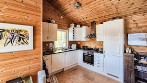 Eine Küchenzeile im Blockhausstil mit Holzwänden, weißen Schränken, einem Herd und einem Fenster.