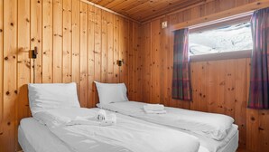 A room with wooden walls, two beds with white linens, a window with curtains, and a small wall-mounted light. - Cozy home in Vøringsfoss with sauna (Vøringsfoss)