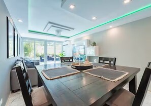 A modern dining area with a dark wooden table, cushioned chairs, and a central decorative piece. - Oceanfront Terrace Apartment - Steps to Beach (Carolina)