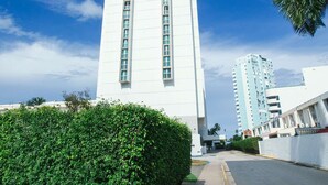 A tall white building with the letters 'esj' on the facade, surrounded by greenery and other buildings. - Oceanfront Terrace Apartment - Steps to Beach (Carolina)