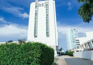 A tall white building with the letters 'esj' on the facade, surrounded by greenery and other buildings. - Oceanfront Terrace Apartment - Steps to Beach (Carolina)