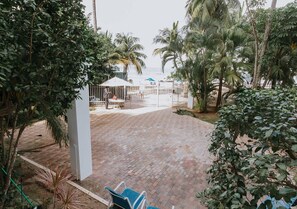 Eine gepflasterte Terrasse mit einem weißen Kiosk, umgeben von Palmen und Blick auf den Strand.