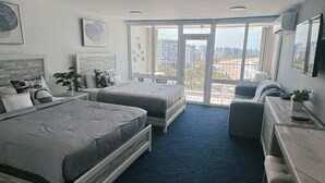 Ein modernes Hotelzimmer mit zwei Betten, einem Sofa, einem Schreibtisch und großen Fenstern mit Blick auf die Stadt.