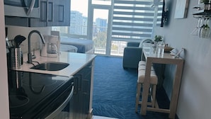 Eine moderne Küche mit Einbauofen, Kaffeemaschine und Spüle. Ein Essbereich mit Tisch und Stühlen bietet Blick durch große Fenster auf die Stadt.