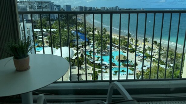 Ein Balkon mit Blick auf einen Strand, einen Poolbereich und umliegende Gebäude.
