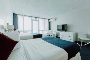 Ein Hotelzimmer mit zwei Betten, einem Schreibtisch, einem Stuhl, einem Fernseher und einem Fenster mit Vorhängen.