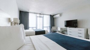 Ett hotellrum med en säng, ett skrivbord, en stol, en tv och en luftkonditioneringsanläggning.