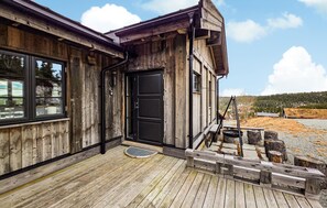 Un bâtiment rustique en bois, doté d’une porte noire, d’une fenêtre et d’une terrasse en bois.
