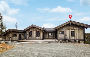 Een houten chalet met een veranda, schoorsteen en een oprit van grind.