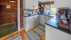 Une cuisine avec des meubles blancs, un plancher en bois et une fenêtre avec des rideaux.