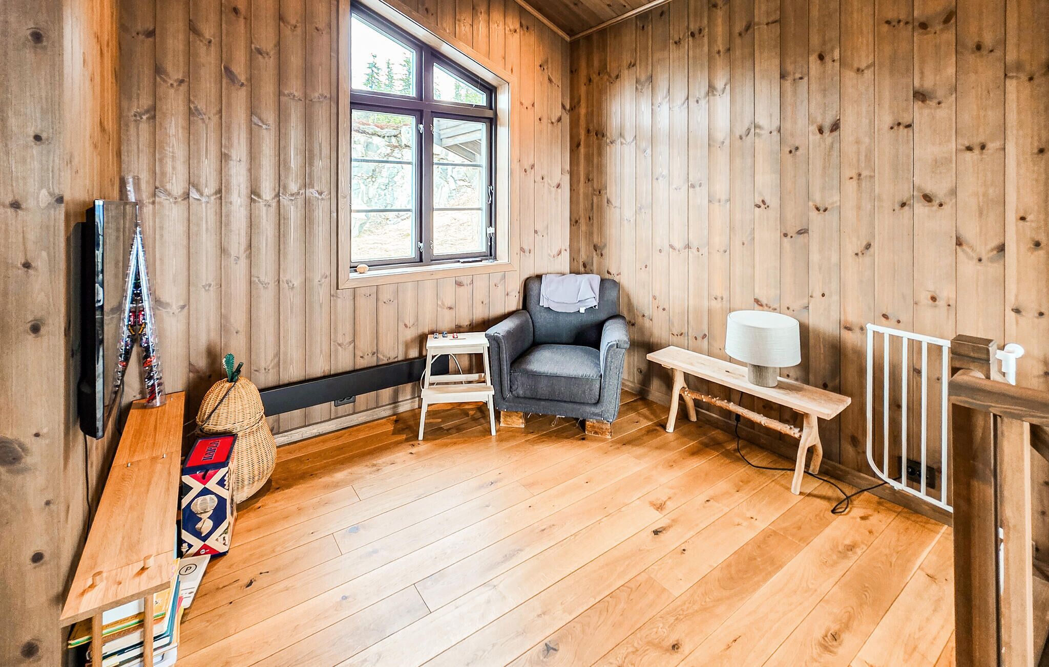 A wooden-paneled room with a window, a chair, a small table, and a lamp.