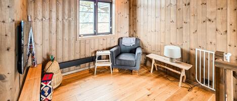 A wooden-paneled room with a window, a chair, a small table, and a lamp.
