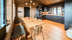 Un intérieur en bois avec une longue table à manger, des chaises, un coin cuisine et une fenêtre.