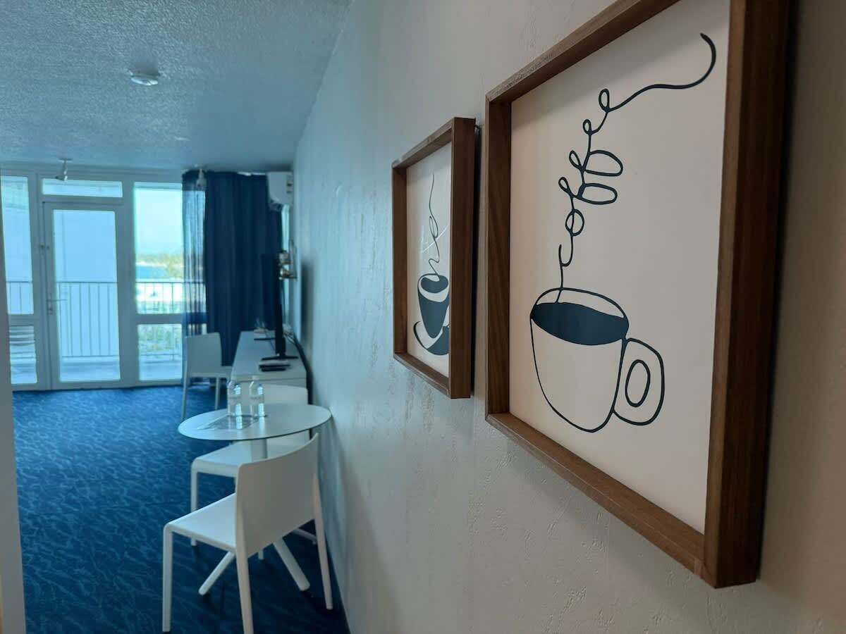 A hotel room with a dining area, a balcony with a view, and framed artwork on the wall.