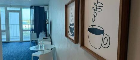 A hotel room with a dining area, a balcony with a view, and framed artwork on the wall.