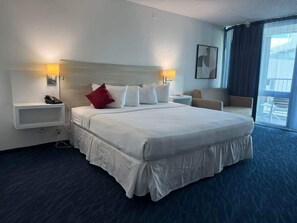 Ein Hotelzimmer mit einem großen Bett, Nachttischlampen, einem Telefon, einem Sessel und Blick ins Freie.