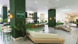 Un espace bar moderne avec des murs d’accent de couleur verte, un comptoir d’accueil et des espaces de détente.