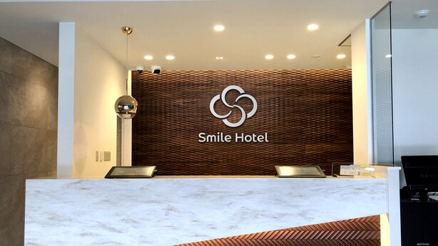 A reception desk with a marble top, a wooden herringbone design, and a logo for Smile Hotel. - Smile Hotel Kanonji (Kanonji)
