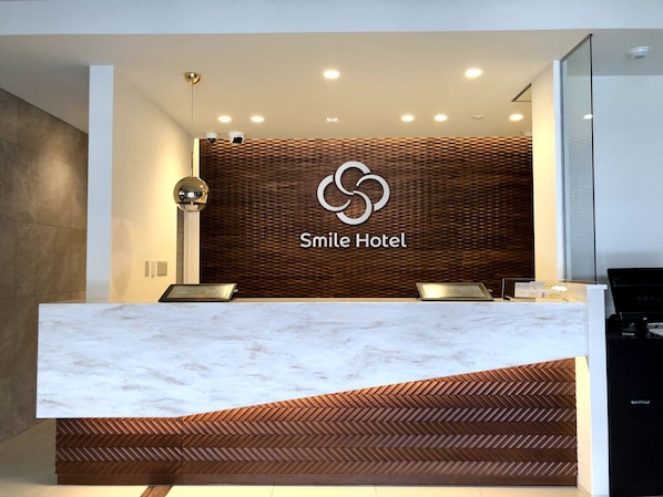 A reception desk with a marble top, a wooden herringbone design, and a logo for Smile Hotel.