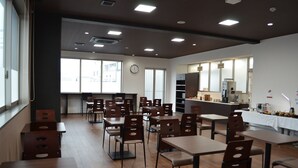 A spacious room with multiple tables and chairs, large windows, and a kitchenette area. - Smile Hotel Kanonji (Kanonji)