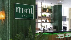 Un espace bar avec un mur texturé de couleur verte, une enseigne indiquant « mont BAR », et un coin salon avec un canapé et des fauteuils.