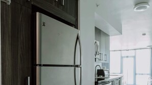 Une cuisine moderne dotée d’un réfrigérateur en acier inoxydable, de meubles de couleur bois foncé et d’un sol carrelé blanc.