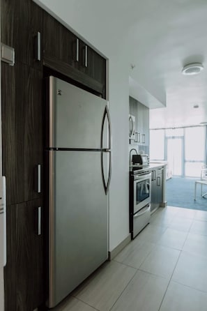 Una cucina moderna con frigorifero in acciaio inossidabile, mobili in legno scuro e pavimento piastrellato di bianco.