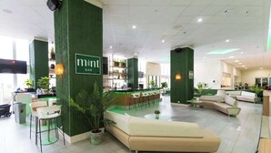 Un hall d’hôtel moderne avec un bar, des espaces aménagés pour s’asseoir et un comptoir de réception.