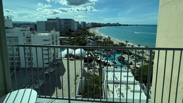 Un balcon avec vue sur une plage, une piscine et les bâtiments avoisinants.