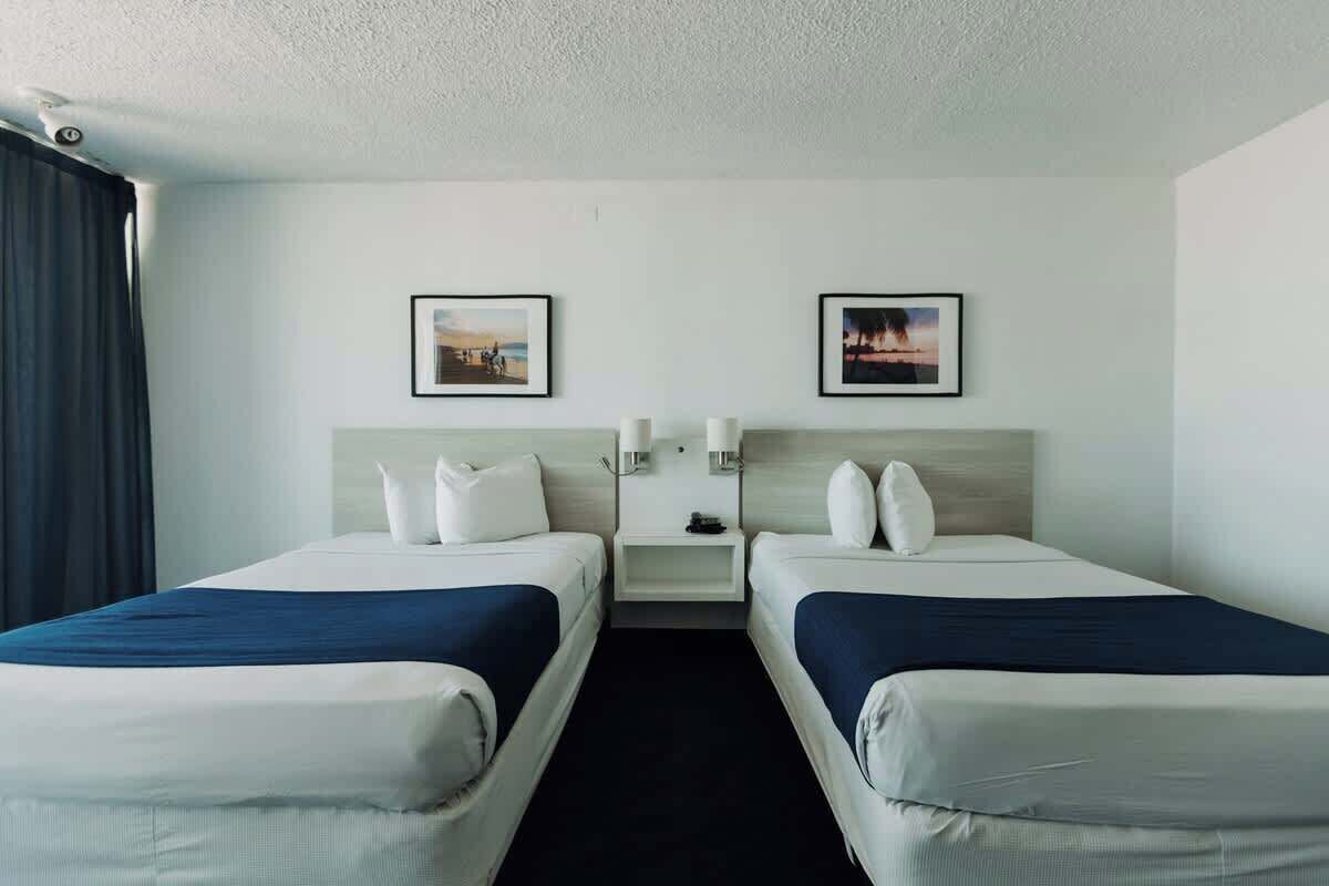 A hotel room with two beds, a nightstand, and two framed pictures on the wall.