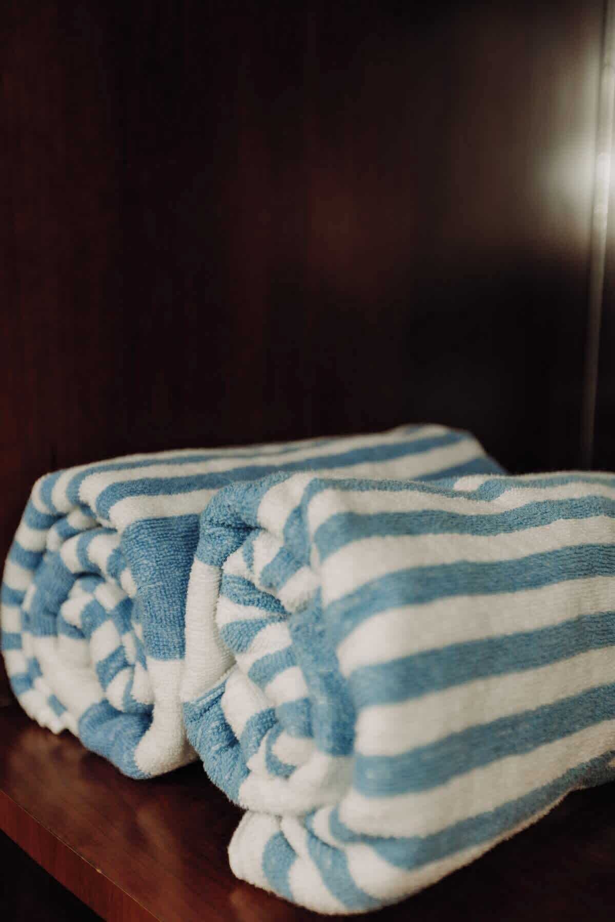 A pair of folded towels with blue and white stripes on a wooden surface.
