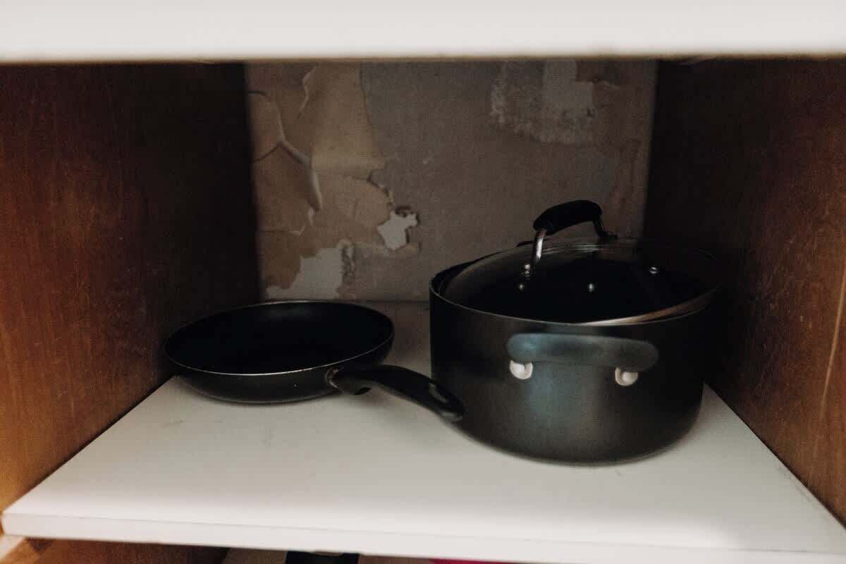 Un coin cuisine avec un plan de travail blanc, une poêle noire et une casserole noire avec un couvercle.
