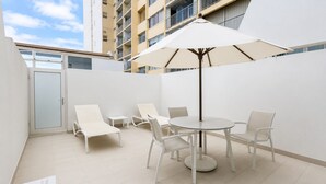 Een terras met een ronde tafel en stoelen, een witte parasol en een deur naar een balkon.